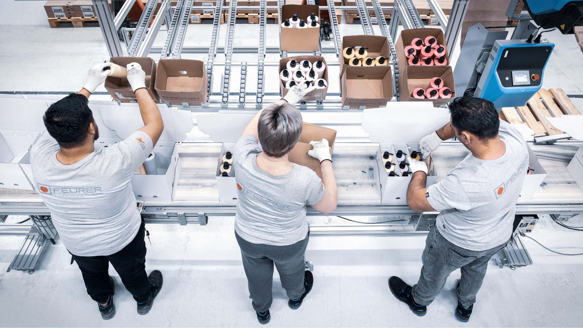 Drei Mitarbeitende montieren und verpacken Produkte an einer modernen Produktionslinie bei FEURER.