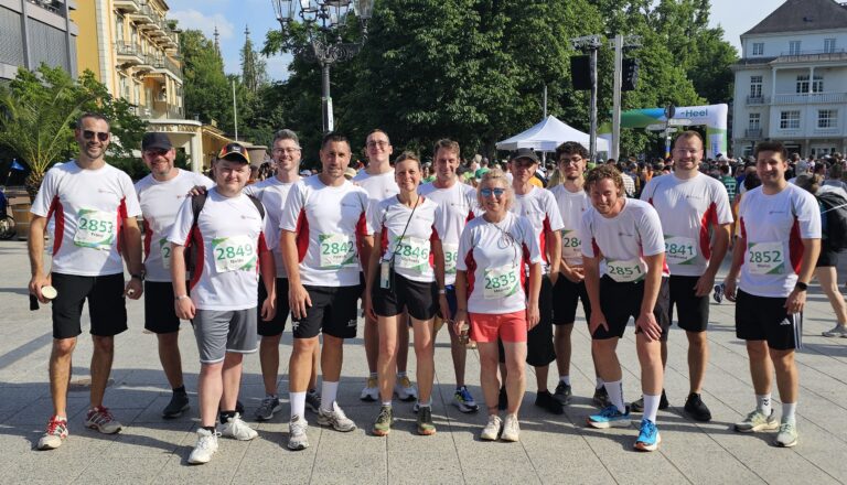 FEURER-Team vor dem Startbereich des 21. HeelLaufs in Baden-Baden. Die Teilnehmenden tragen FEURER-Laufshirts und Startnummern und posieren gemeinsam für ein Gruppenfoto.